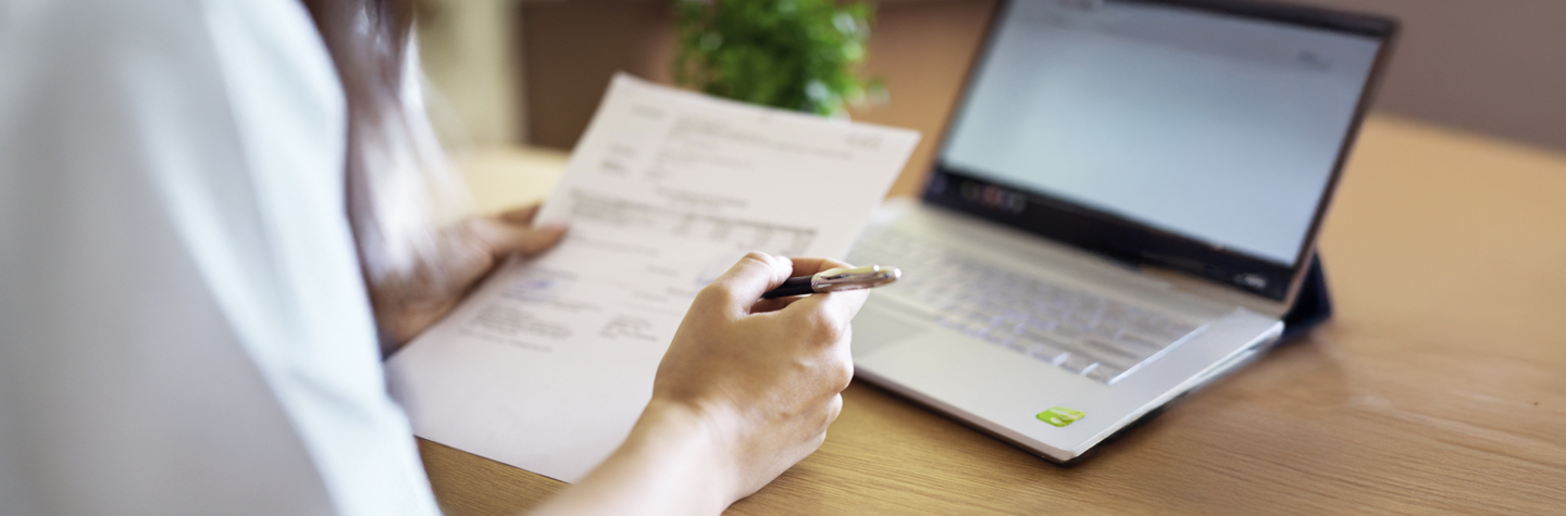 Persona escribiendo notas en un cuaderno mientras mira datos en una pantalla de computadora